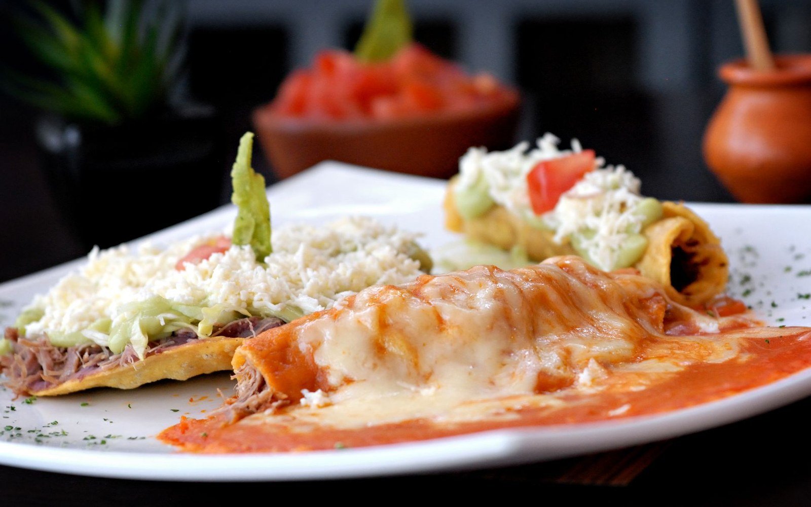 Cheese-topped enchiladas in red sauce served with tostadas and rolled tacos