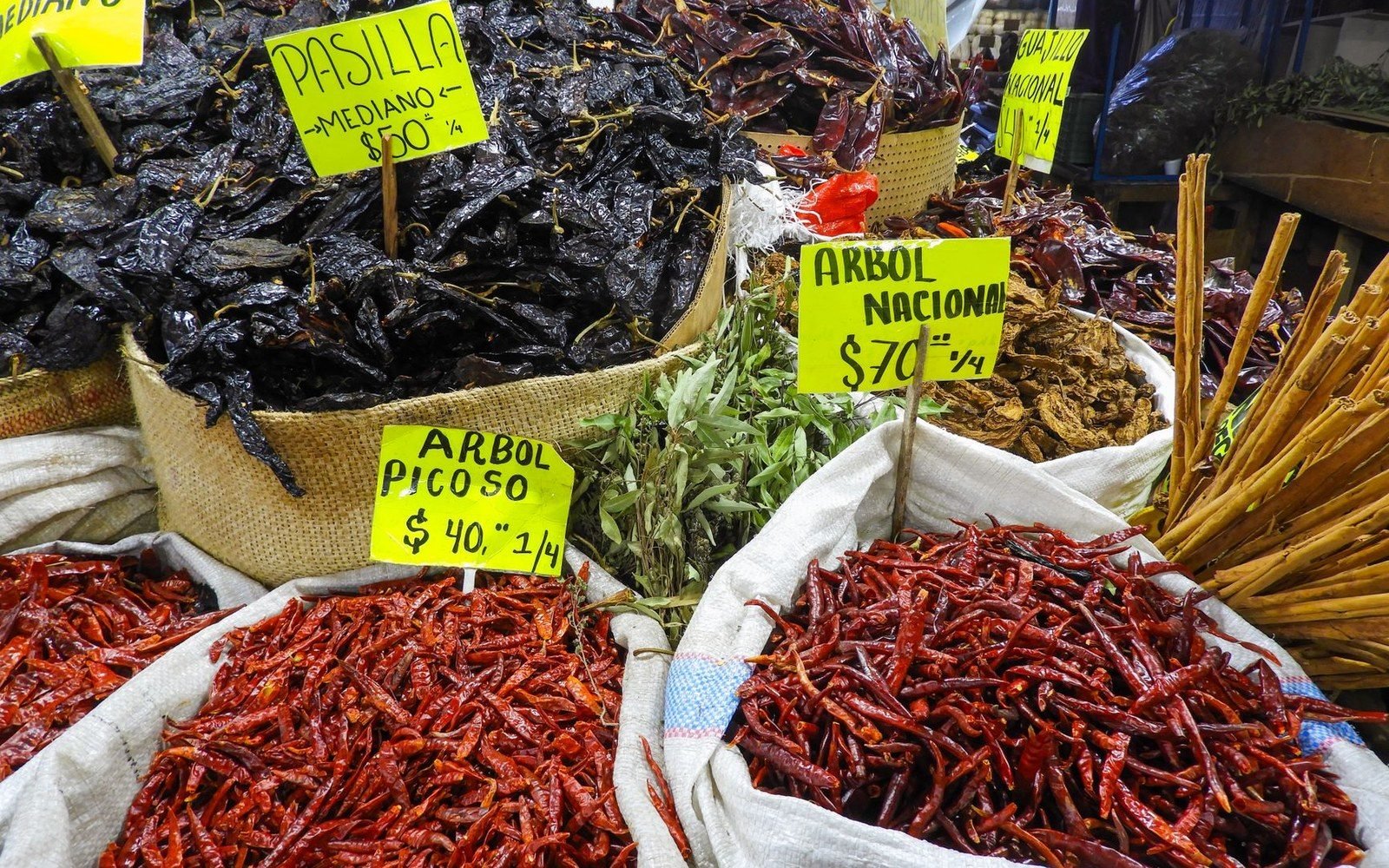 Sacks of dried pasilla and arbol chiles with handwritten price signs at a market stall