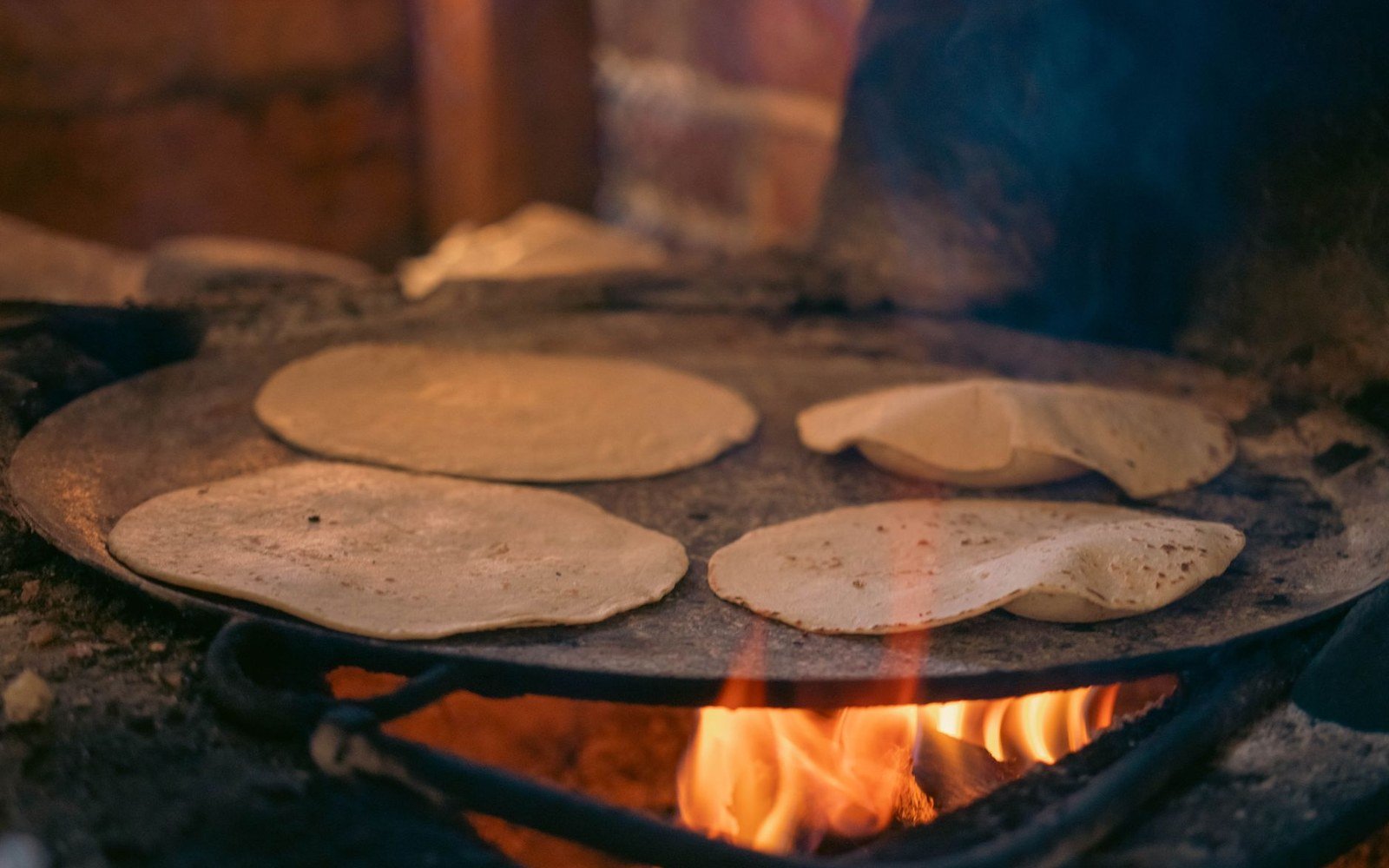 Corn tortillas cooking on a flat griddle over an open wood fire