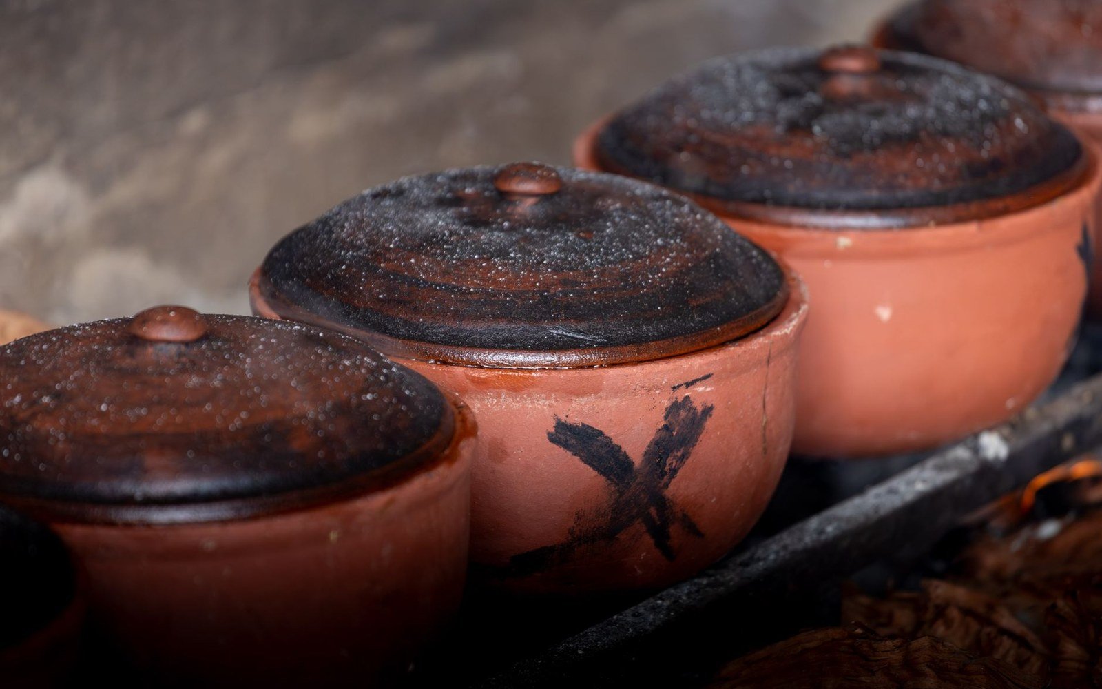 Row of lidded clay pots with soot-blackened tops sitting over an open fire