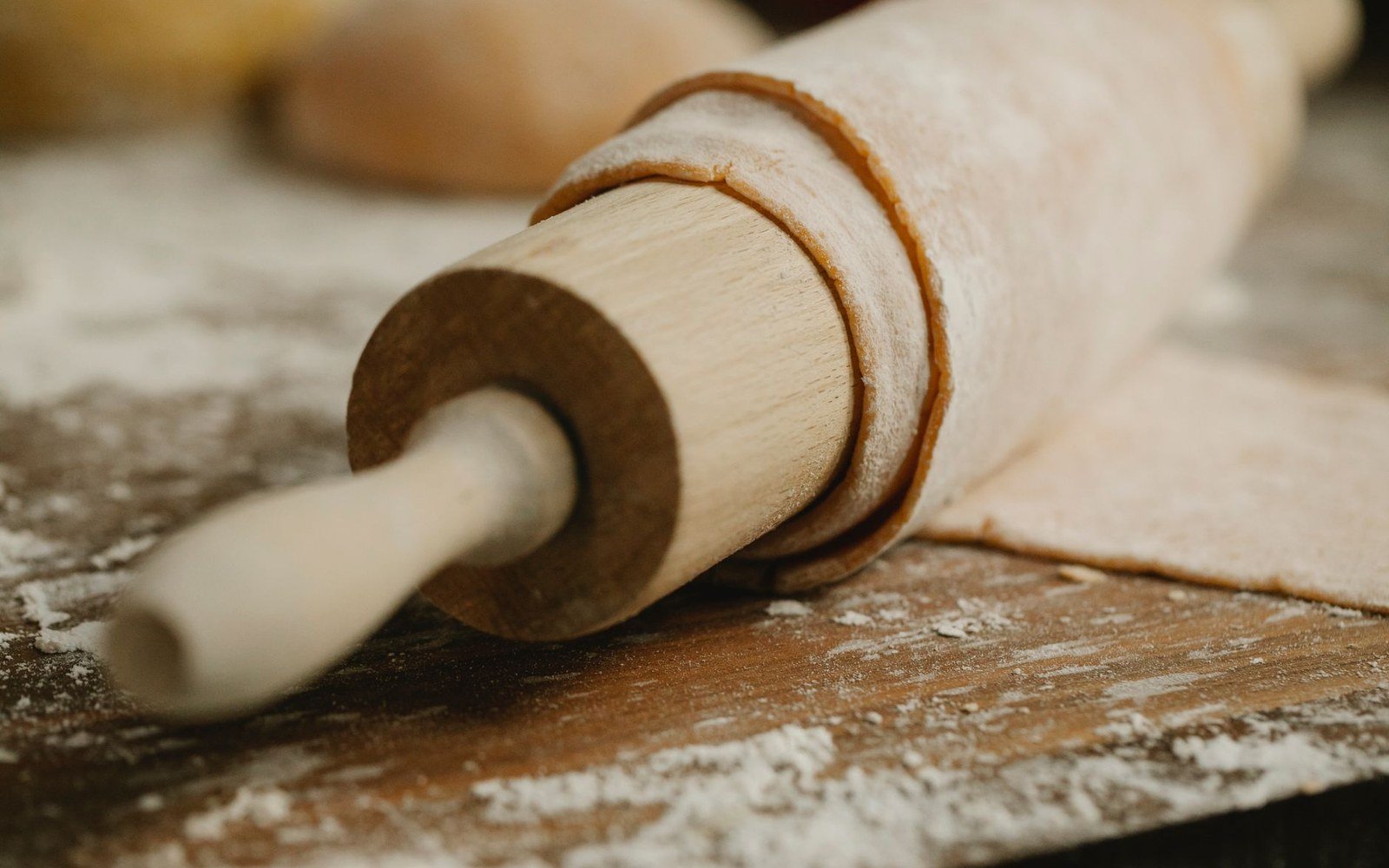 Wooden rolling pin wrapped in flour-dusted dough on a floured surface
