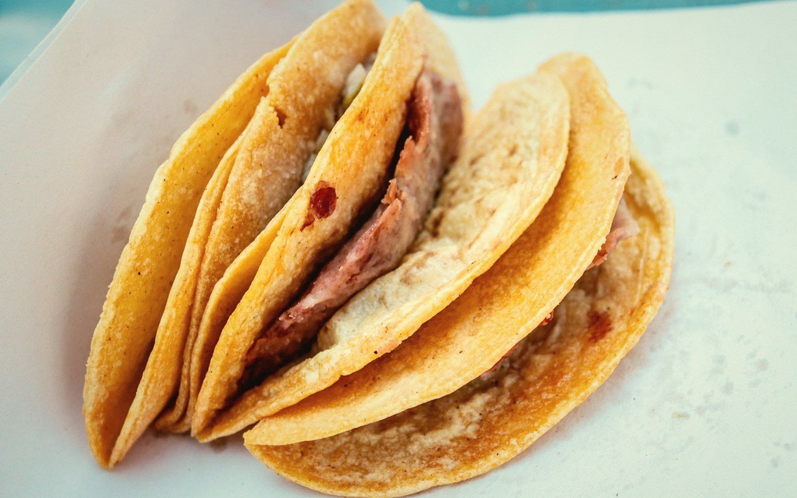 Several folded corn tortilla tacos filled with meat stacked on a white plate