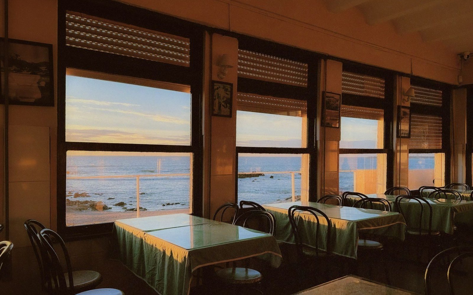 Empty seaside restaurant with green tablecloths overlooking the ocean at sunset through large windows