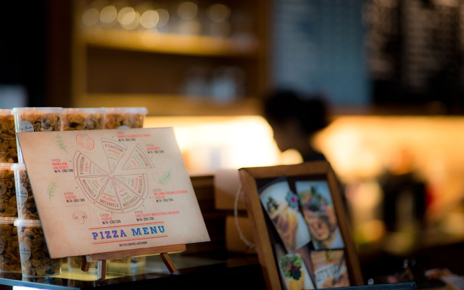 Pizza menu card on a café counter with stacked snack containers nearby