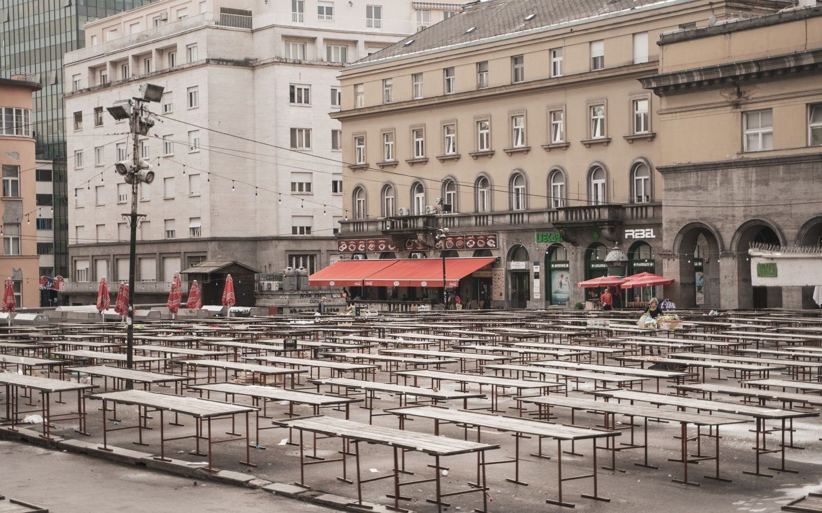 Empty market square lined with rows of vacant wooden tables and folded umbrellas