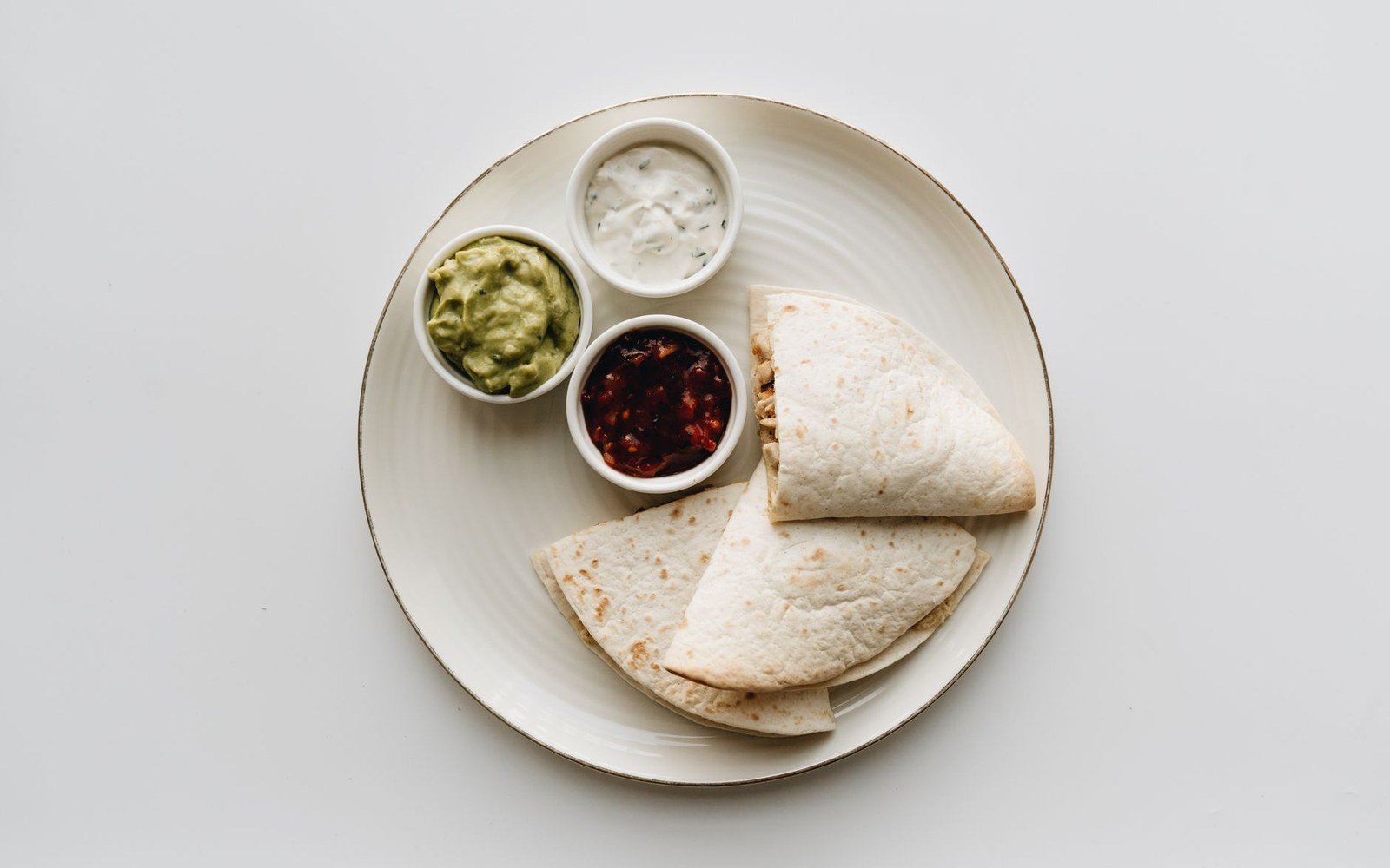 Folded quesadilla wedges on a plate with guacamole, sour cream and salsa