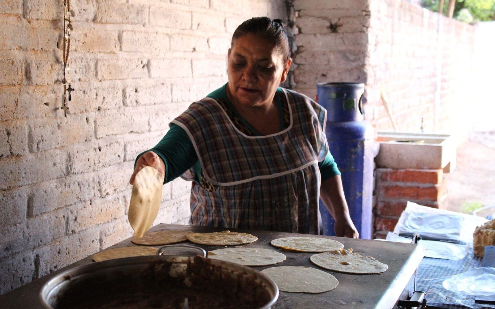 Woman flipping fresh tortillas on a metal griddle in an outdoor kitchen