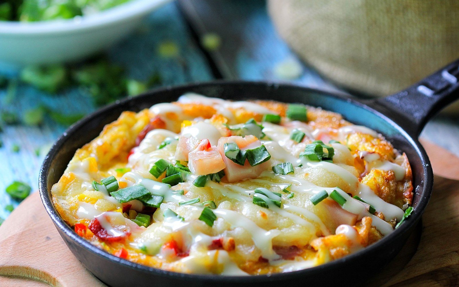 Cheesy skillet dish topped with green onions and drizzled with sauce